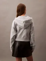 Buzo gris con capucha, cierre frontal con cremallera, logo de Calvin Klein bordado en el pecho y corte cropped.