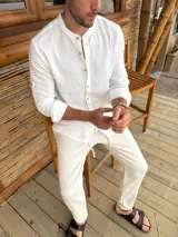 Camisa de cuello mao en color blanco, confeccionada en tela liviana con textura. Presenta cierre frontal con botones de madera y mangas largas con puños arremangados.