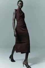 Vestido midi de cuello subido y sin mangas, con detalle de drapeado lateral en el delantero. Presenta un diseño entallado y cierre posterior con cremallera oculta.