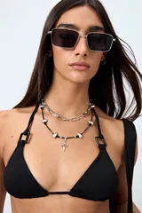 Top de bikini negro confeccionado en tejido con textura, de diseño triangular y detalle de aros cuadrados en los breteles. Se ajusta en cuello y espalda con lazos finos.