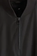 Campera bomber negra, de corte estándar, con cuello elevado acanalado, cierre frontal y bolsillos laterales con cierre. Presenta puños y bajo con ribete acanalado ancho.