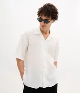 Camisa de lino blanca de corte boxy, manga corta, cuello bowling y cierre frontal de botones.