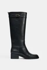 Bota de caña alta estilo hípica, color negro, con detalle de tira decorativa con hebilla metálica en la parte superior. Presenta tacón bajo ancho y punta redonda.
