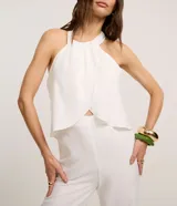 Mono largo blanco de crepé, con cuello halter, sin mangas y superposición fruncida en el tronco. Se ata con lazo en la nuca.