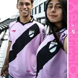 Camiseta de fútbol rosada con una banda diagonal negra que cruza el pecho. En la banda se encuentra el escudo del club y cuatro estrellas doradas.