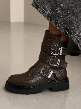 Bota tipo borcego de cuero color marrón oscuro, con suela track negra y tres correas horizontales con hebillas metálicas plateadas.