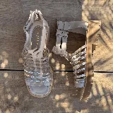 Sandalias bajas de cuero color beige con tiras horizontales plateadas y cierre con hebilla al tobillo.