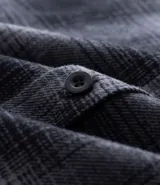 Camisa masculina de franela a cuadros en tonos grises y negros, con capucha con cordón ajustable, cierre frontal abotonado y mangas largas.