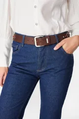 Cinturón de cuero marrón con hebilla metálica plateada, detalle de aros metálicos laterales y pasador con logo grabado.