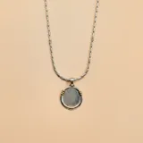 Collar de cadena de eslabones de plata con detalles en oro, que sostiene un dije circular de plata con borde decorado en oro.