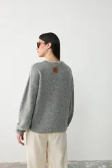 Sweater de tejido bouclé color gris, con cuello en V profundo y bolsillo frontal tipo canguro, ambos con detalles de borde en color crema. Presenta mangas largas y un corte holgado.