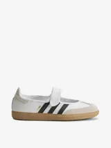 Zapatillas Adidas modelo Samba Jane, con diseño tipo Mary Jane. Presentan una capellada de cuero blanco con las icónicas tres tiras laterales en negro, puntera de gamuza en tono beige y suela de goma tipo gum. Incluyen una tira con cierre de velcro en el empeine.