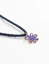 Collar con cordón azul marino y dije de flor calada con incrustaciones de strass azul y rojo.