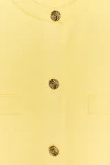 Chaqueta de punto color amarillo pálido, con cuello redondo, manga corta, cierre frontal con botones dorados y bolsillos de parche en el pecho.