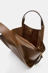 Bolso bandolera de formato city color marrón, con diseño estructurado, pespuntes decorativos, doble asa de mano y cremalleras laterales con tiradores colgantes.
