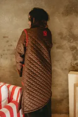 Campera larga acolchada color marrón, con diseño matelassé, detalles de piel sintética en el cuello y puños, y bordados artesanales en crochet color rojo en los bolsillos y costuras.