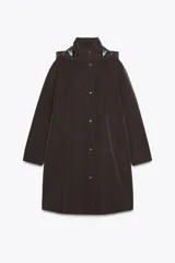 Chubasquero largo color marrón oscuro, con cuello subido y capucha ajustable con cordones. Tiene cierre frontal con cremallera oculta y botones a presión, y bolsillos delanteros con solapa y botón a presión oculto.