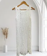 Vestido largo sin mangas, color blanco, con tejido de punto abierto y textura ondulada. Presenta un escote redondo y un ruedo con terminación festoneada.