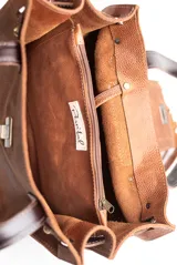 Cartera tipo tote de cuero color beige con diseño de flecos en la solapa frontal. Cuenta con manijas de cuero oscuro, cierre metálico tipo torniquete y detalles de herrajes dorados.