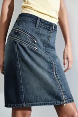 Falda de denim azul con tiro medio, cierre frontal completo con cremallera y detalles de bolsillos falsos con cremalleras en la parte delantera.