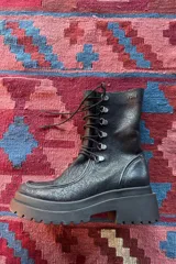 Borcego de caña corta confeccionado en cuero negro, con diseño de cordones y ganchos metálicos, cierre lateral y suela de plataforma dentada.