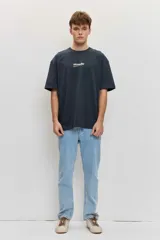Remera de corte oversize color blanco tiza, de manga corta y cuello redondo, con pequeño estampado gráfico azul en el pecho.