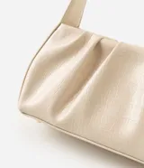 Cartera tipo baguette de marca Satinato, confeccionada en material sintético de poliuretano con textura crocco en color beige. Cuenta con diseño estructurado, cierre en cremallera con herrajes dorados y asa fija de hombro.