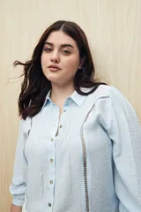 Camisa blanca de manga larga con cuello clásico y botones de nácar. Presenta detalles calados en el frente.