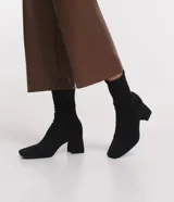 Bota de caña corta tipo media marca Satinato, color negro, con punta cuadrada y tacón grueso de altura media, confeccionada en material textil elástico sin cierre.