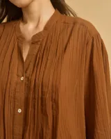 Túnica o camisa larga color blanco hueso, confeccionada en algodón, con cuello mao, frente abotonado y pliegues verticales en el pecho.