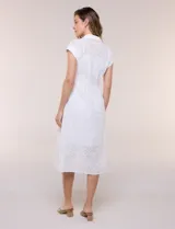 Vestido midi blanco estilo camisero de la marca Julia Jordan, confeccionado en tejido broderie 100% algodón. Presenta cuello camisero tradicional, cierre frontal con botones, mangas cortas con vuelta y cintura entallada con pinzas que da paso a una falda evasé. Cuenta con forro interior.