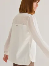 Camisa de corte recto y manga larga, confeccionada en algodón. Presenta un diseño combinado con un panel superior en la espalda de tela bordada con motivos florales y el resto de la prenda en tela lisa, con detalle de costuras a contratono en el ruedo.