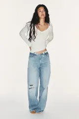Jeans de mezclilla de tiro medio, corte wide leg y diseño relaxed. Presenta detalles rotos y desgastados en las piernas, y una cinturilla doblada superpuesta con trabillas y cierre frontal con cremallera y botón metálico.