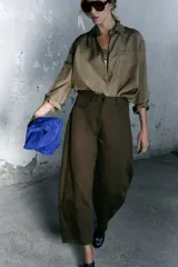 Pantalón de tiro medio color verde oliva, confeccionado en tejido con estructura de espiga. Presenta pierna ancha, trabillas en la cintura, cinco bolsillos y cierre frontal con cremallera y botón.