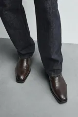 Bota marrón de cuero con estampado de cocodrilo, corte a la altura del tobillo, punta fina y cierre lateral con cremallera.