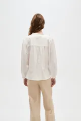 Blusa de viscosa color blanco, con cuello en V, detalles de volados y frunces en el frente, y mangas largas abullonadas con puños ajustados.