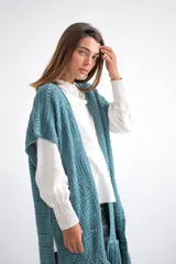 Chaleco largo de tejido de punto color azul verdoso, sin mangas y con flecos en el ruedo. Presenta calados con diseño geométrico.