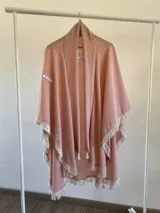 Ruana de tela fina color rosa con terminaciones de flecos en color crema en todo su borde.