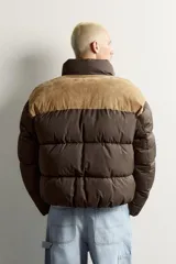 Cazadora puffer relaxed fit color marrón con canesú superior en tono tostado de acabado aterciopelado. Cuenta con cuello subido, manga larga, bolsillos de vivo en la cadera, acabados en elástico y cierre frontal con cremallera.