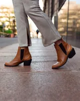 Botinetas de gamuza en tono beige con paneles elásticos laterales negros y detalle de aplique en cuero marrón en el talón. Presentan un taco cuadrado de altura media y punta redondeada.