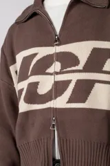 Campera tejida de punto con cierre frontal completo y cuello polo. Presenta un diseño con franja horizontal en color azul y letras en blanco sobre fondo negro, con puños y ruedo acanalados.