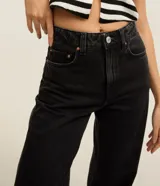 Pantalón wide leg de jean negro, tiro alto, con bolsillos delanteros y traseros, presillas en la cintura y cierre frontal con botón y cremallera.