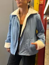 Campera de jean celeste con interior y cuello de corderito color crema, cierre frontal con cremallera y bolsillos laterales.