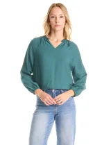 Blusa de satén color verde petróleo, con escote en V y cuello decorado con mostacillas bordadas. Presenta mangas largas con puños elásticos y ruedo también elastizado, brindando un ajuste cómodo y holgado.