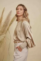 Blusa de satén color champagne con cuello a la base, mangas anchas y puños elásticos con detalle bordado.