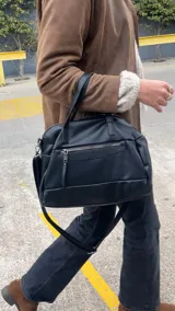 Cartera de mano y hombro color beige, de material símil cuero, con forma estructurada y redondeada. Posee dos asas cortas superiores y una correa larga ajustable y desmontable. Cuenta con un bolsillo exterior con cierre en la parte frontal.