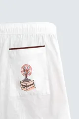 Bermuda de corte relajado confeccionada en algodón, color blanco con vivo en contraste color marrón en el ruedo. Presenta cintura elástica con cordón ajustable y un bordado decorativo en la pierna derecha que incluye una palmera y un gallo.