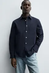 Camisa de corte regular fit confeccionada en tejido de algodón con textura. Presenta cuello solapa, cierre frontal de botones, manga larga con puños abotonados y un bolsillo plastrón en el pecho.