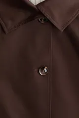 Chaqueta corta de sarga marrón con cuello camisero, manga raglán y cierre frontal de botones. Cuenta con bolsillos laterales y cordón ajustable en el bajo, con detalles de forro a rayas en los puños y el interior.
