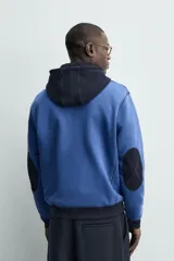 Sudadera hoodie regular fit de color azul, con capucha y bolsillo canguro negro. Cuenta con cordones ajustables blancos y detalles en color negro en la capucha, el bolsillo y los puños.